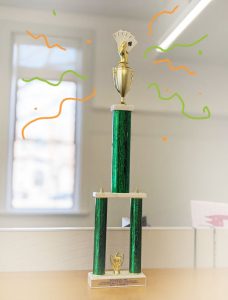 A green and gold trophy with a gold hand holding cards at the top.