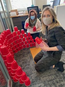 Lindsay and Jess building a wall out of red solo cups in front of Brian's office