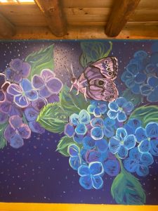 Painting of a pink butterfly perched on blue flowers